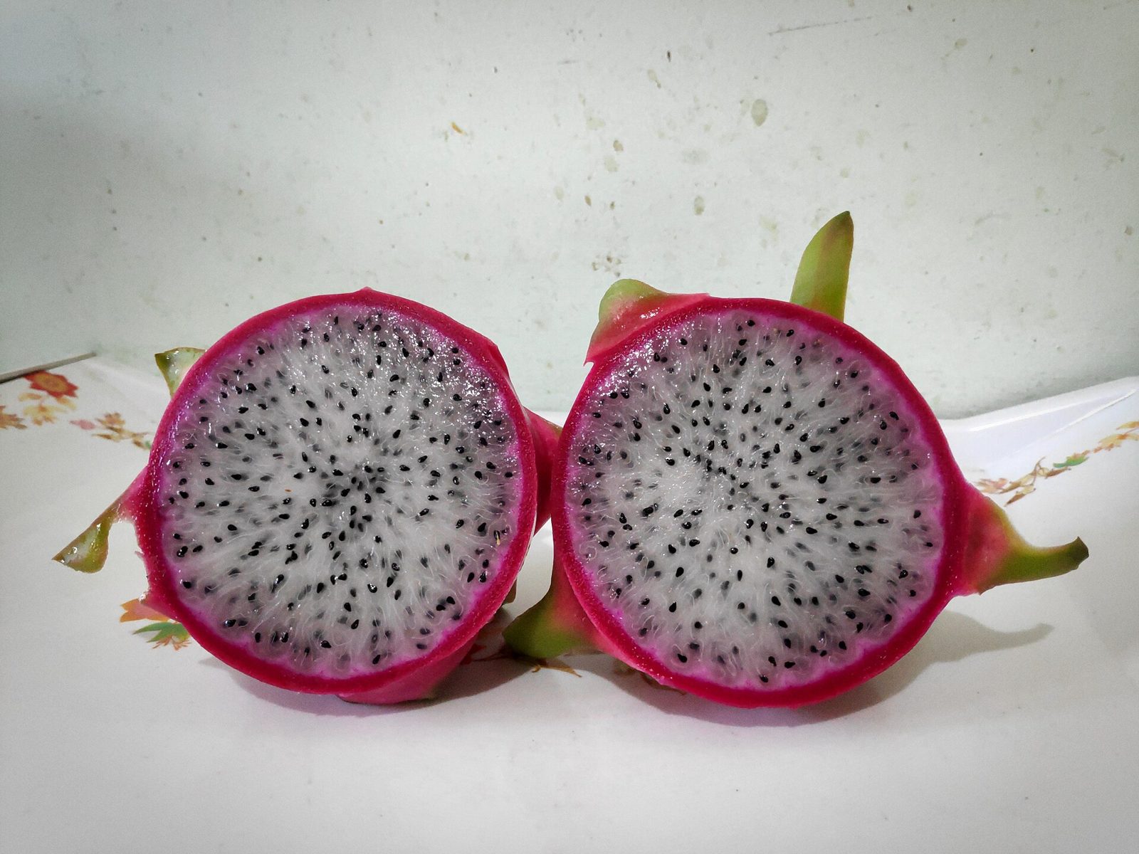 Two halves of a dragon fruit standing cut side forward, showing white flesh speckled with small black seeds inside a bright magenta rim