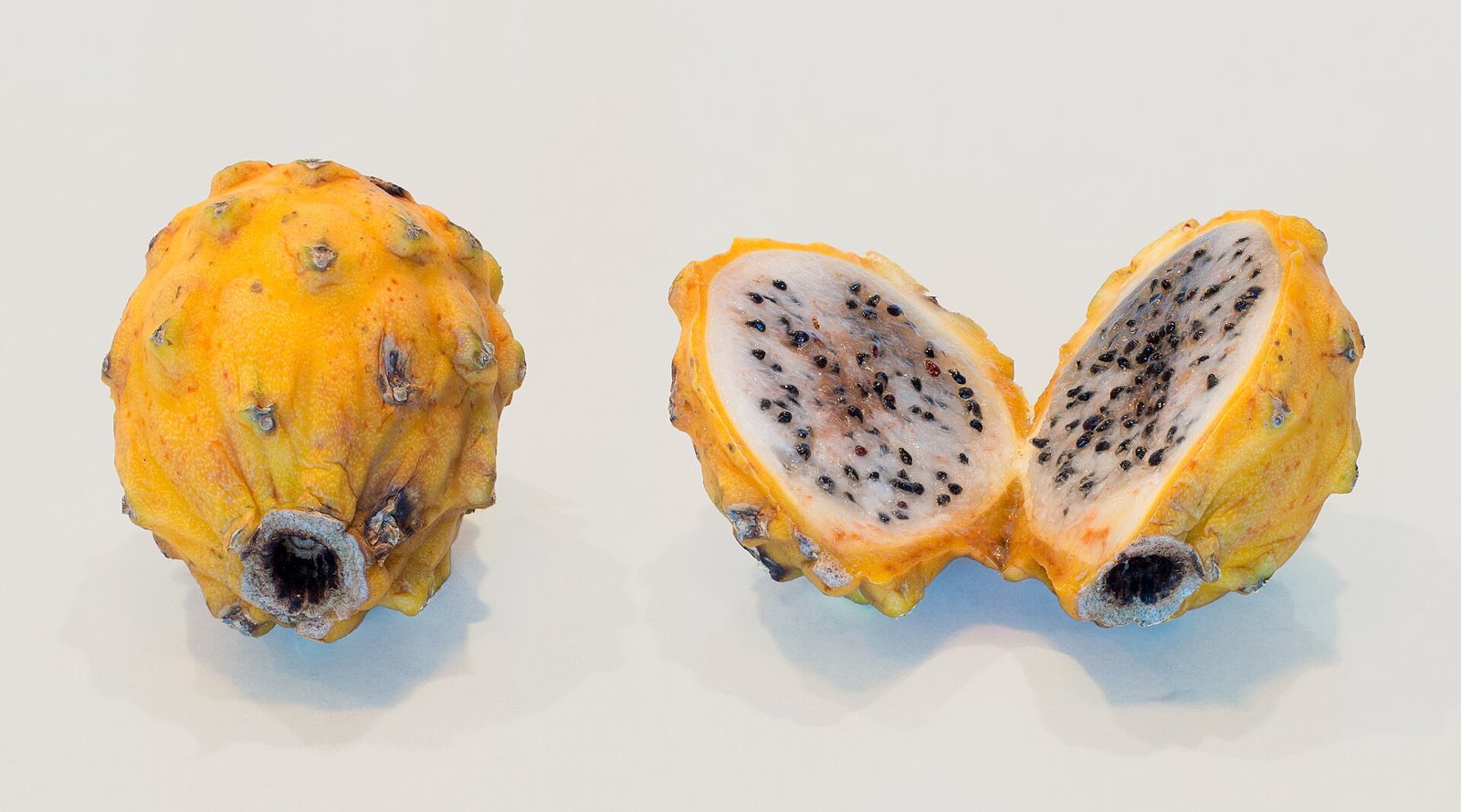 Two yellow dragon fruits with knobby skin, one whole and one cut open to show translucent white flesh with black seeds