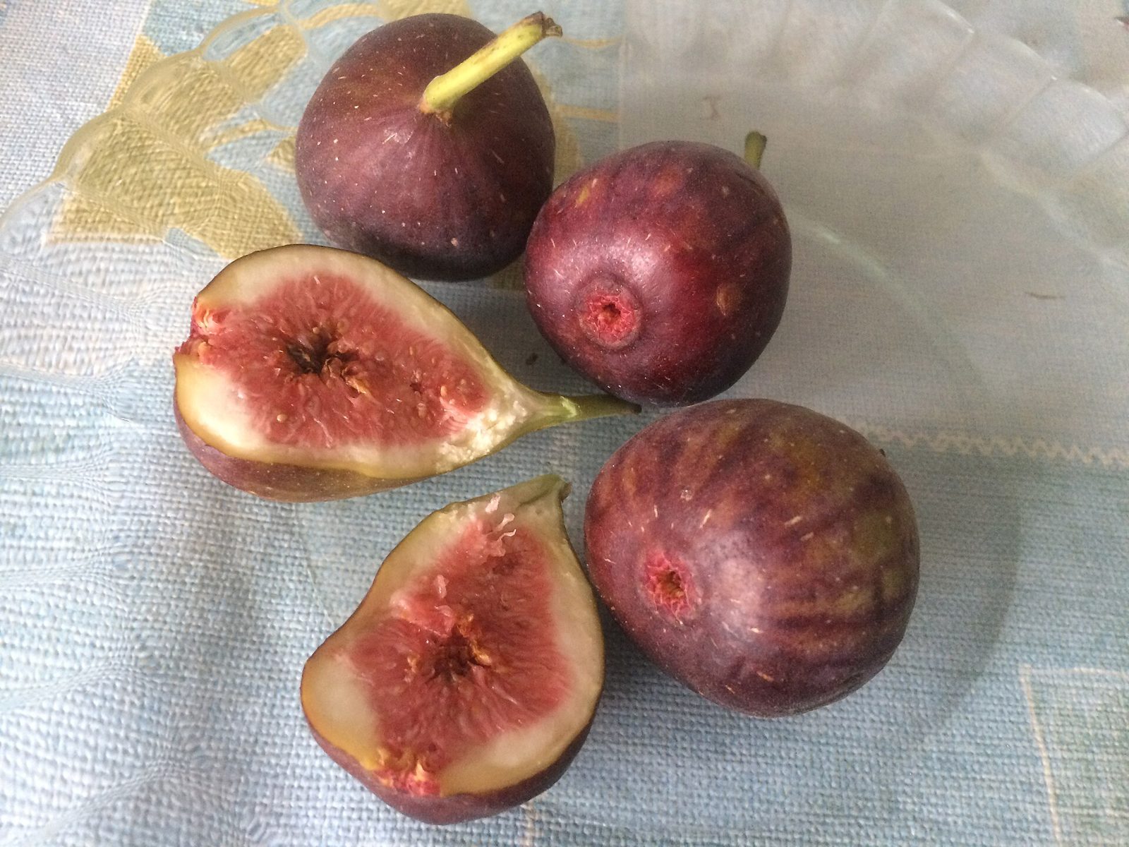Whole and halved purple-brown figs on a plate, with the pinkish flesh and seeds visible inside