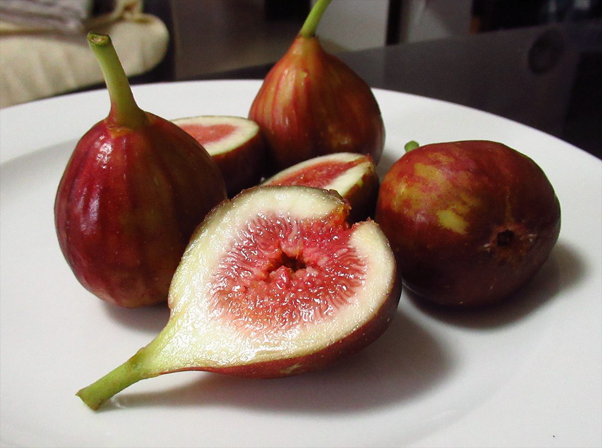 Whole and halved red-purple striped figs on a white plate, showing pink flesh and seeds