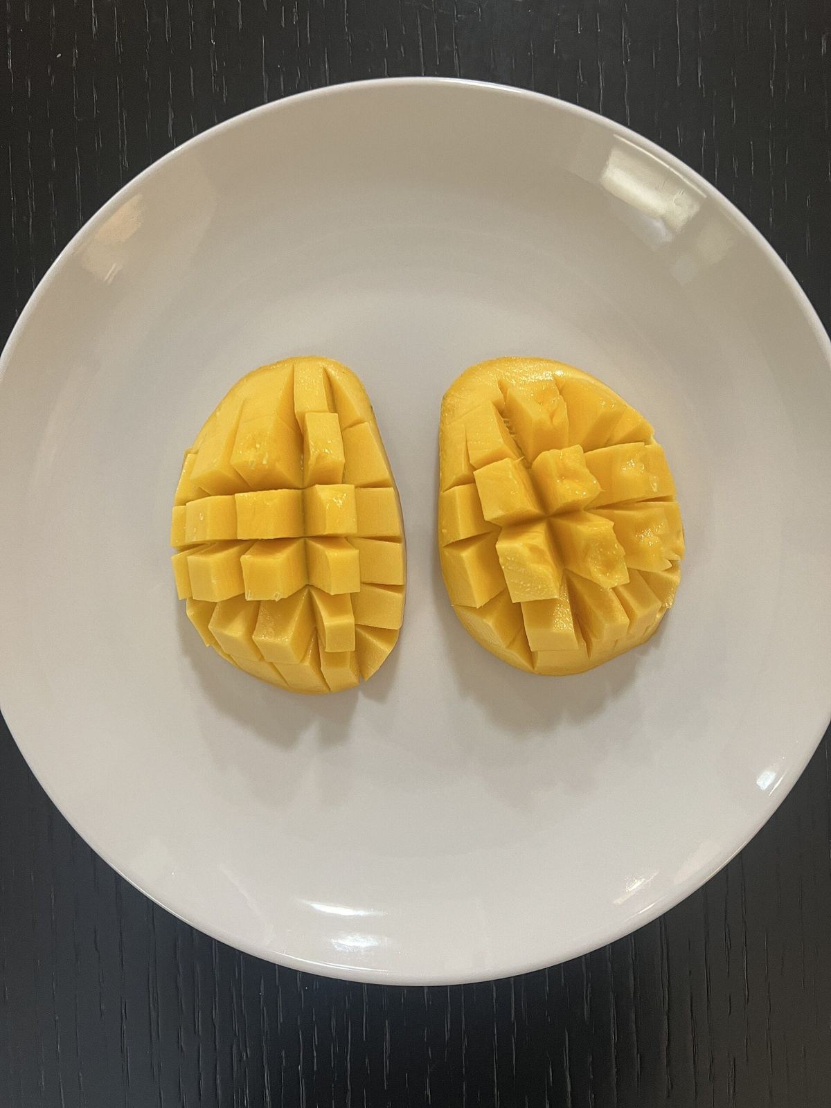 Two mango cheeks scored into cubes, hedgehog style, on a white plate